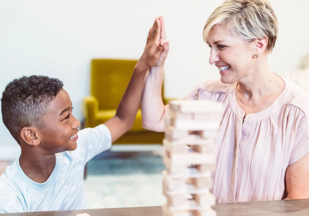 une éducatrice avec un enfant qui se tapent dans la main car ils ont réussi leur jeu